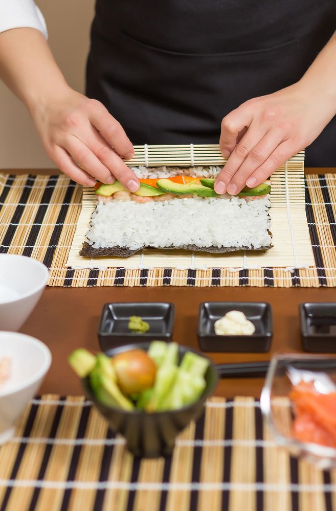 Hands of woman chef arranging filling in rice to roll sushi in a nori seaweed sheet, vertical