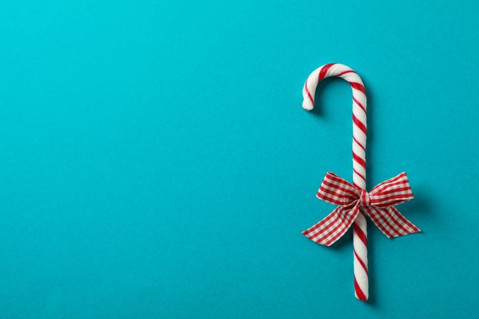 Sweet candy cane with bow on turquoise background, space for text