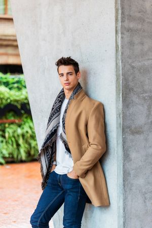 Handsome man wearing camel coat and scarf looking at camera against cement