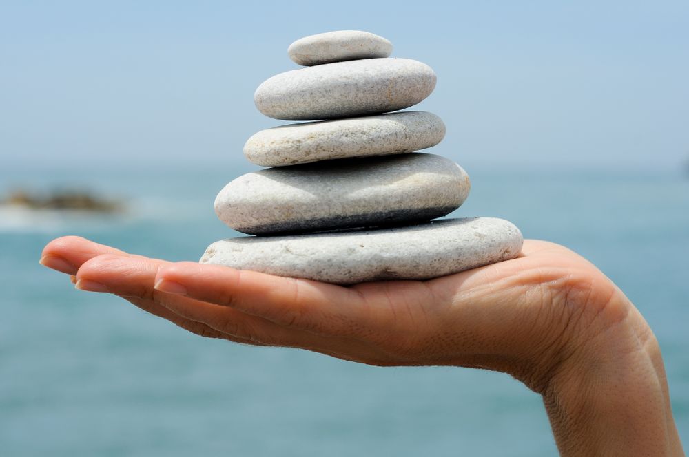 Side view of hand with small pile of rocks with sea in background