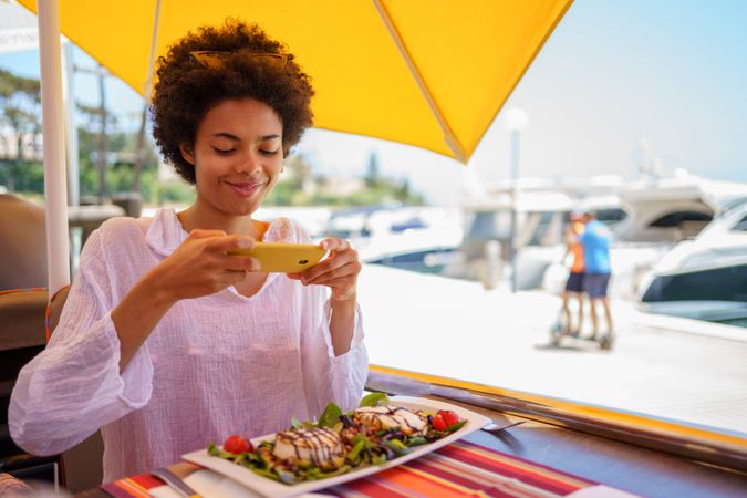 Happy woman using phone take picture of meal at waterfront cafe