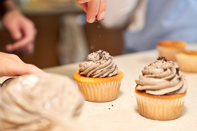 Crop woman decorating cupcakes with chocolate