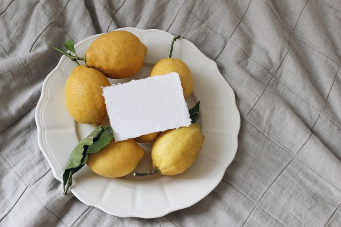 Fresh yellow lemons, dry green leaves on plate with blank card