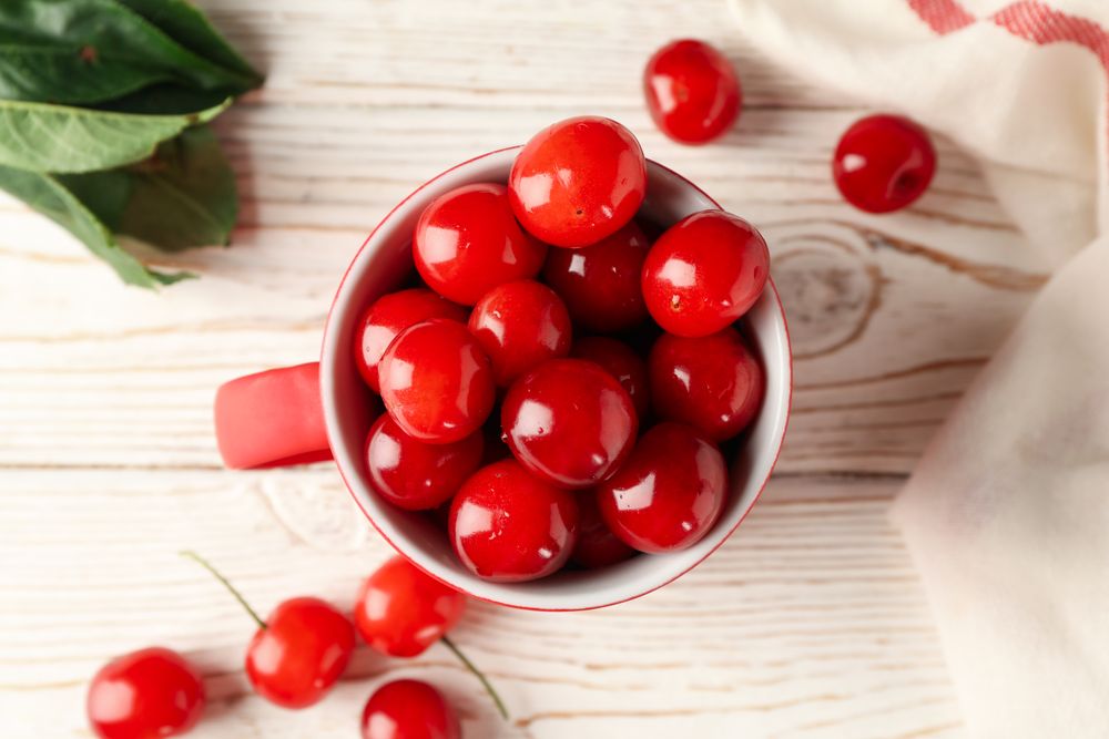 Cup with cherry and towel on wooden background, top view