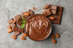 Bowl with chocolate and chocolate pieces on gray background