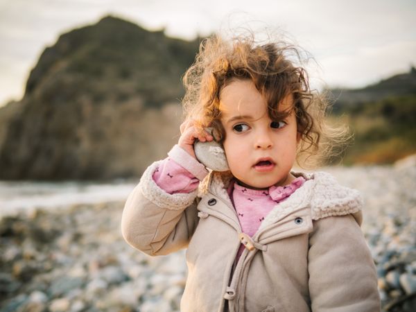 Toddler girl playing with seashell on beach