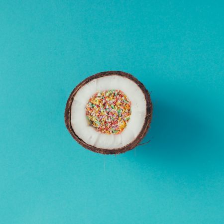 Coconut half full of colorful sprinklers on blue background