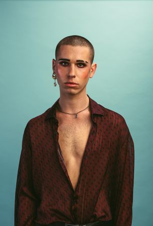 Young man wearing makeup standing at studio with blank expression