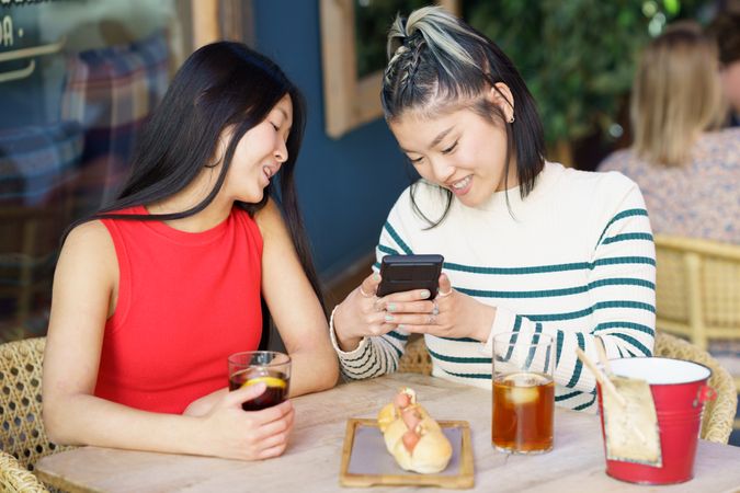 Two women sitting in restaurant patio using their phone to take picture of their food