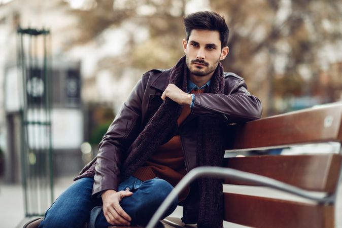 Man in leather coat sitting on outside bench