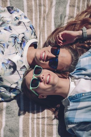 Two women with sunglasses smiling lying in blanket
