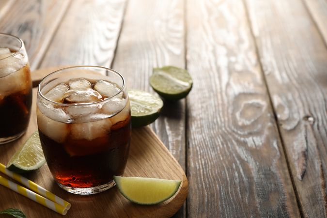 Glasses with ice cola, lime slices and tubules on wooden background