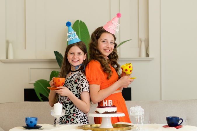 Two girls back-to-back in birthday hats