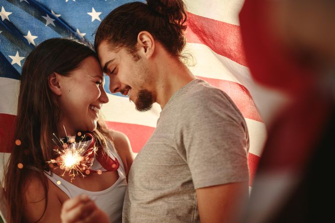 Loving couple holding sparklers wrapped under American flag