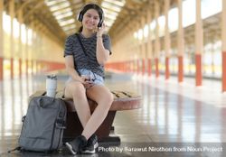 A young woman sits and listens to music while waiting for a train to travel 5oYqgb