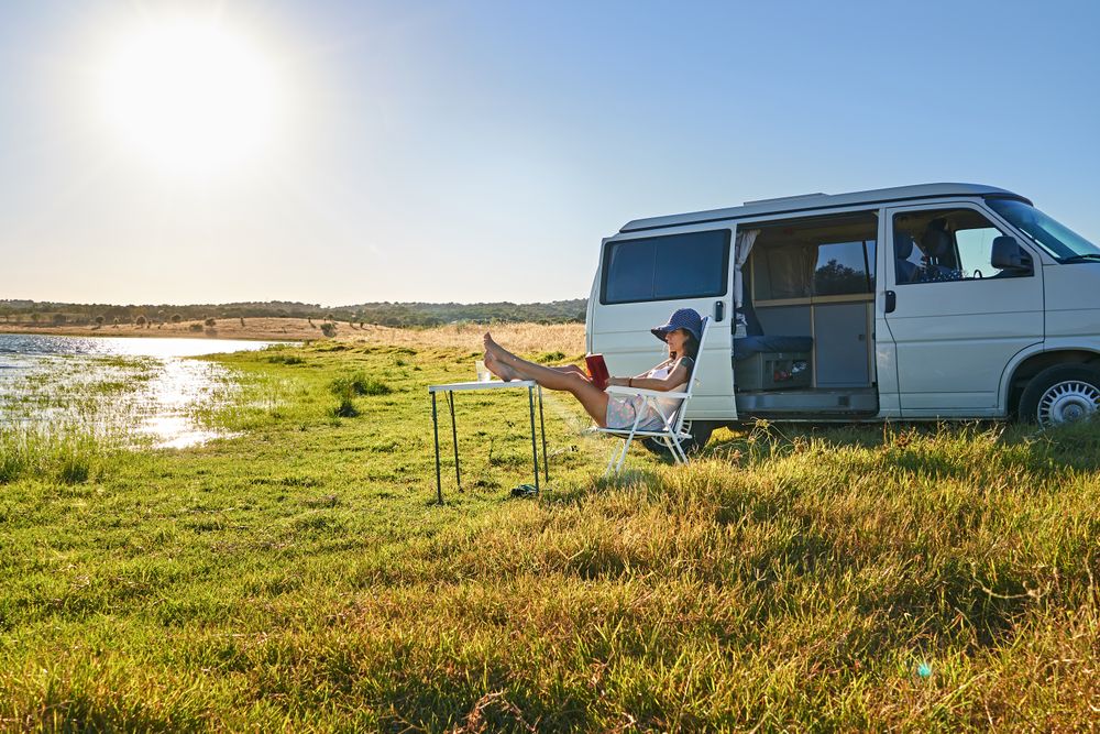 Woman sitting on chair near table and reading book on shore of river