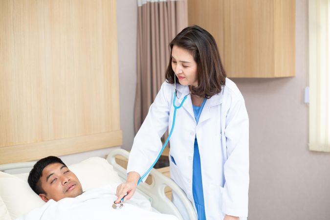 Asian female doctor visit male patient sleeping on bed