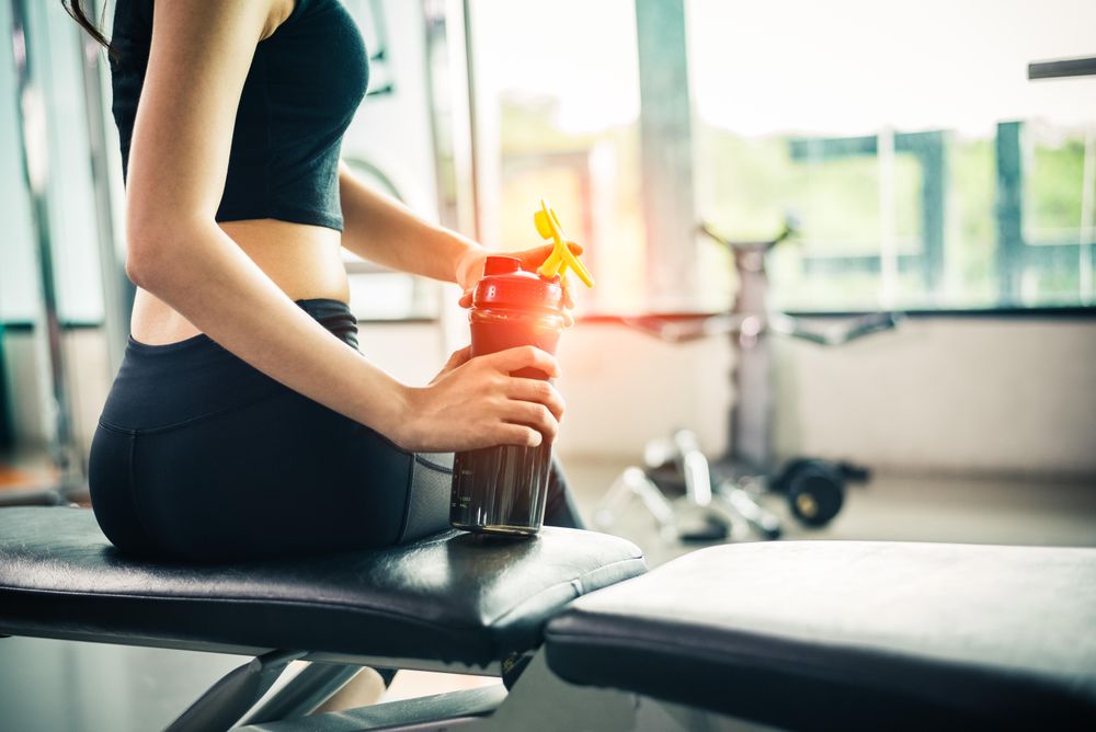 Anonymous female sitting on gym bench with drink