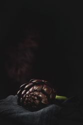 Fresh raw purple artichokes on dark background.