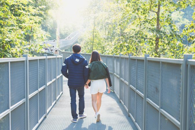 Back view of young man and woman holding hands and walking on bridge