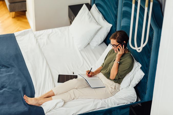 Businesswoman taking notes from a phone call on hotel bed
