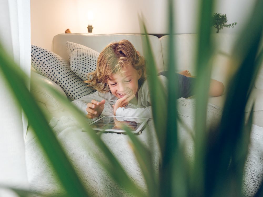 Preteen boy lying on sofa and playing on tablet