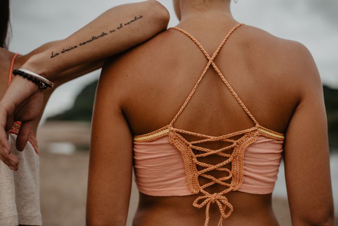 Anonymous tattooed woman leaning on friend on beach