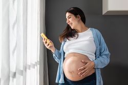 Pregnant woman browsing smartphone at home