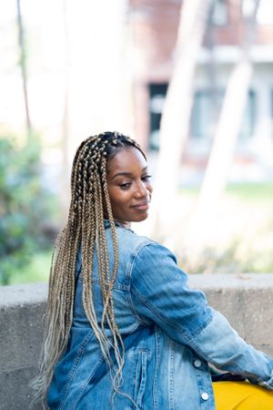 Woman sitting outside with blonde box braids and denim jacket looking back