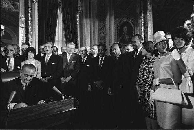 President Lyndon Johnson signs the Voting Rights Act as Dr. Martin Luther King, Jr looks on