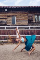 Flexible woman in colorful skirt dancing at rural paddock