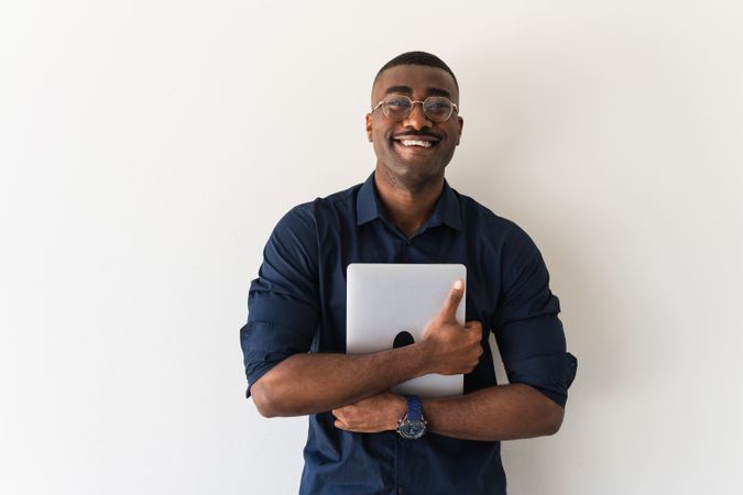 Smiling Black guy with laptop near white wall