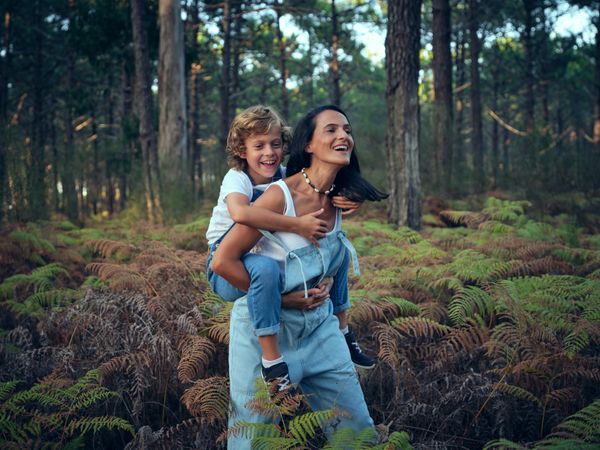 Son riding back of mother during walk in woods