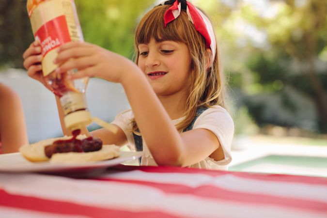 Little girl pouring ketchup on her grilled hotdog