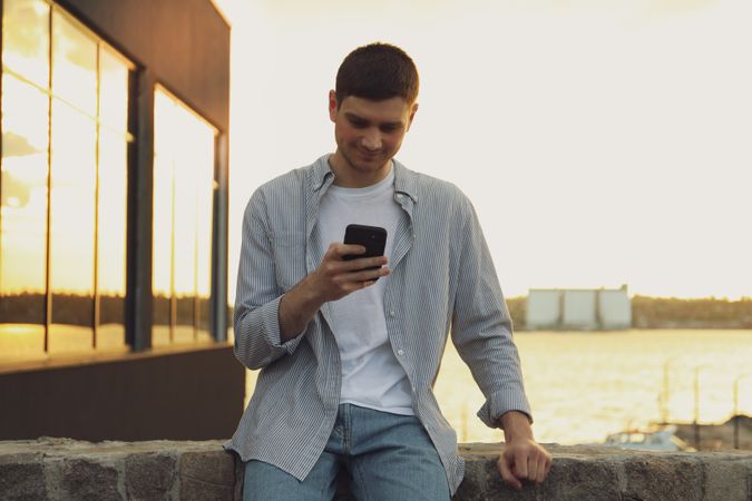 Young man uses a phone outdoor. Writing a message