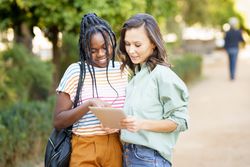 Women friends pointing at something on tablet in casual clothing outside