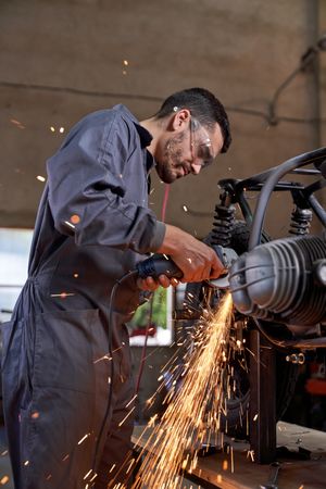 Male mechanic in workwear repairing motorbike in garage