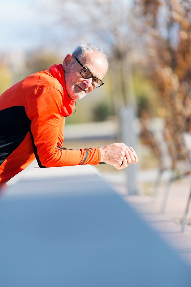 Older male leaning on wall in park and looking at camera