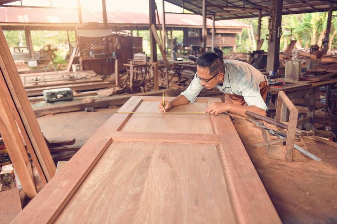 Carpenter taking measurements of wooden door on table