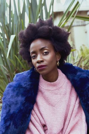 Woman in pink sweater and blue fur coat sitting beside green plant