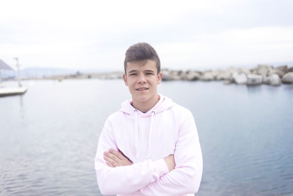 Young male teenager with crossing arms standing on the coast while looking at camera