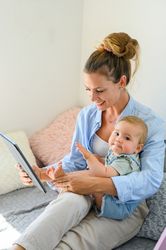 Cheerful woman with baby and tablet on bed