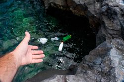 Crop man pulling plastic bag out of water