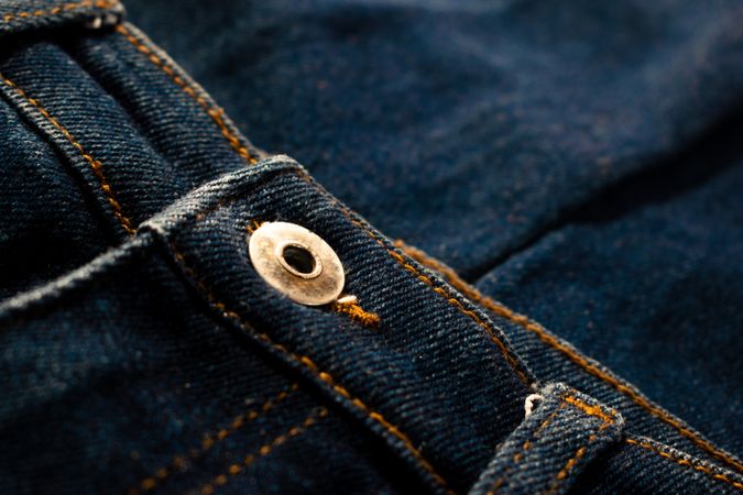 Close up gold and shiny button navy blue jeans fabric background texture.