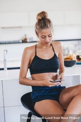 Young woman sitting in kitchen and using mobile phone 0VV130