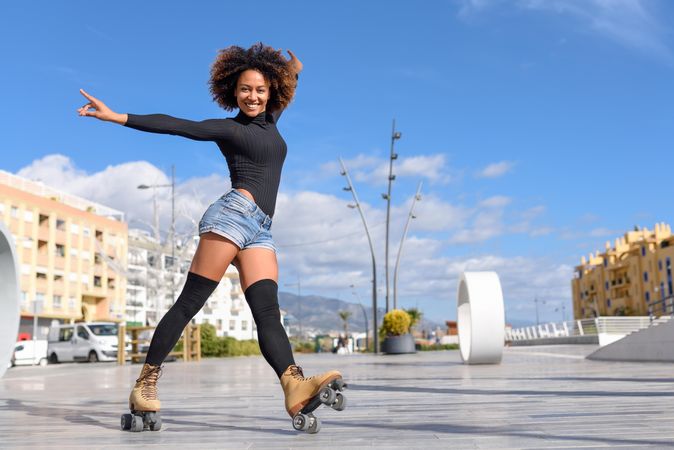 Side view of happy woman with afro roller skating outside