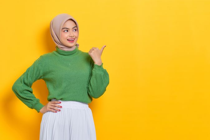 Happy woman in headscarf pointing her thumb to the side