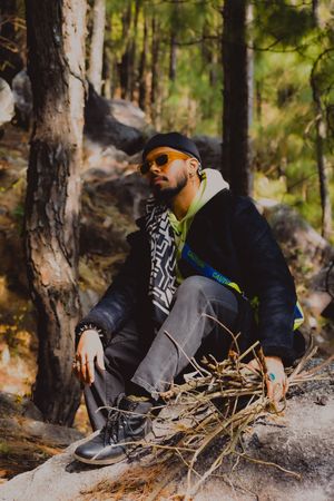 Man in casual outwear with sunglasses sitting on ground beside a tree