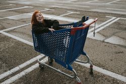 Smiling woman sitting in shopping trolley in parking lot
