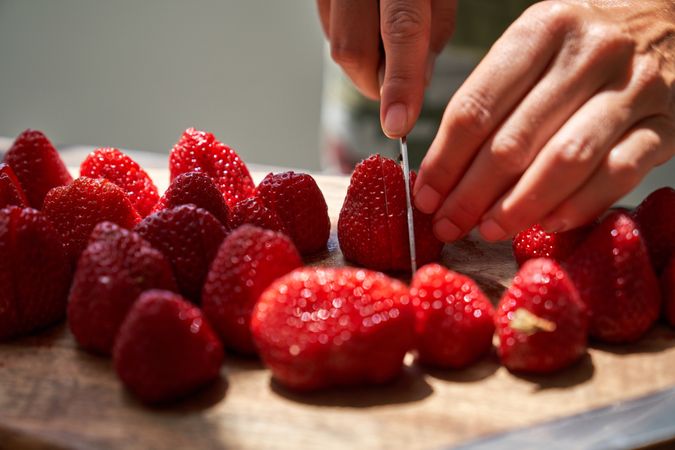 Crop person cutting strawberry on wooden table